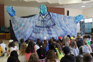 enormous puppet overlooks students in assembly